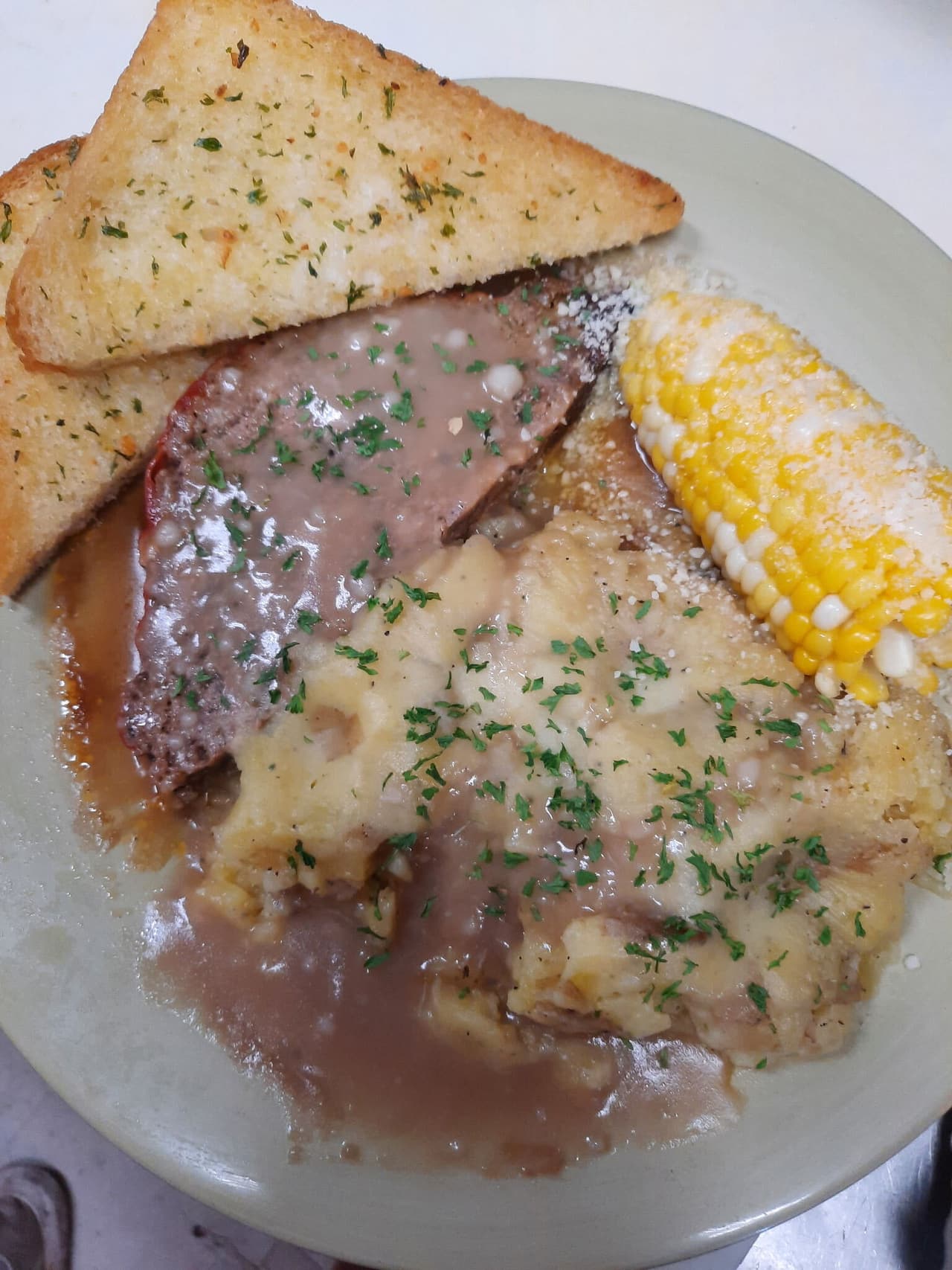 Home-cooked dinner plate with gravy, corn on the cob and garlic toast