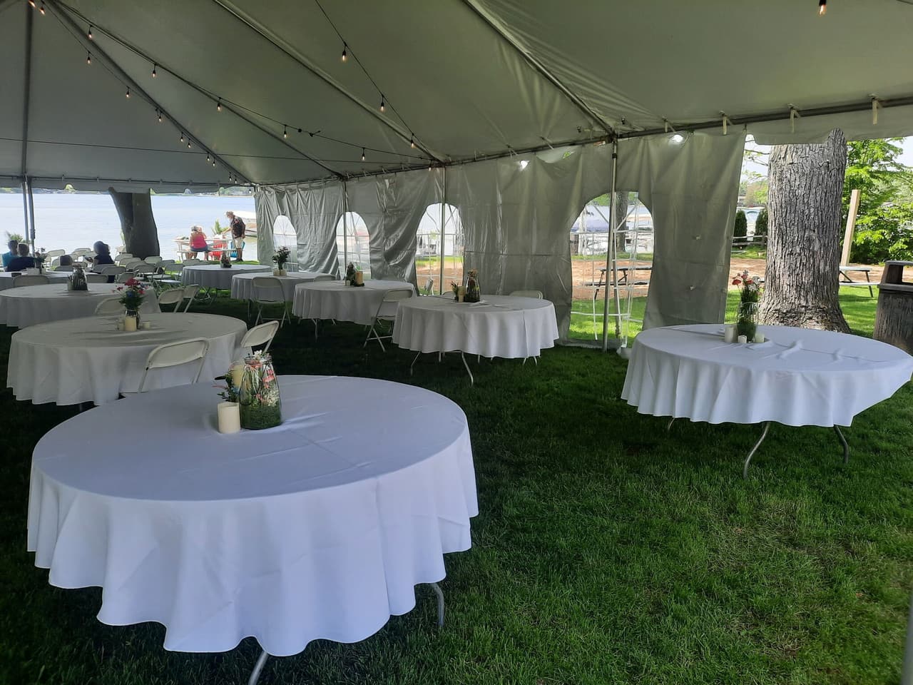 Round tables with white cloths set up under a tent on the lawn