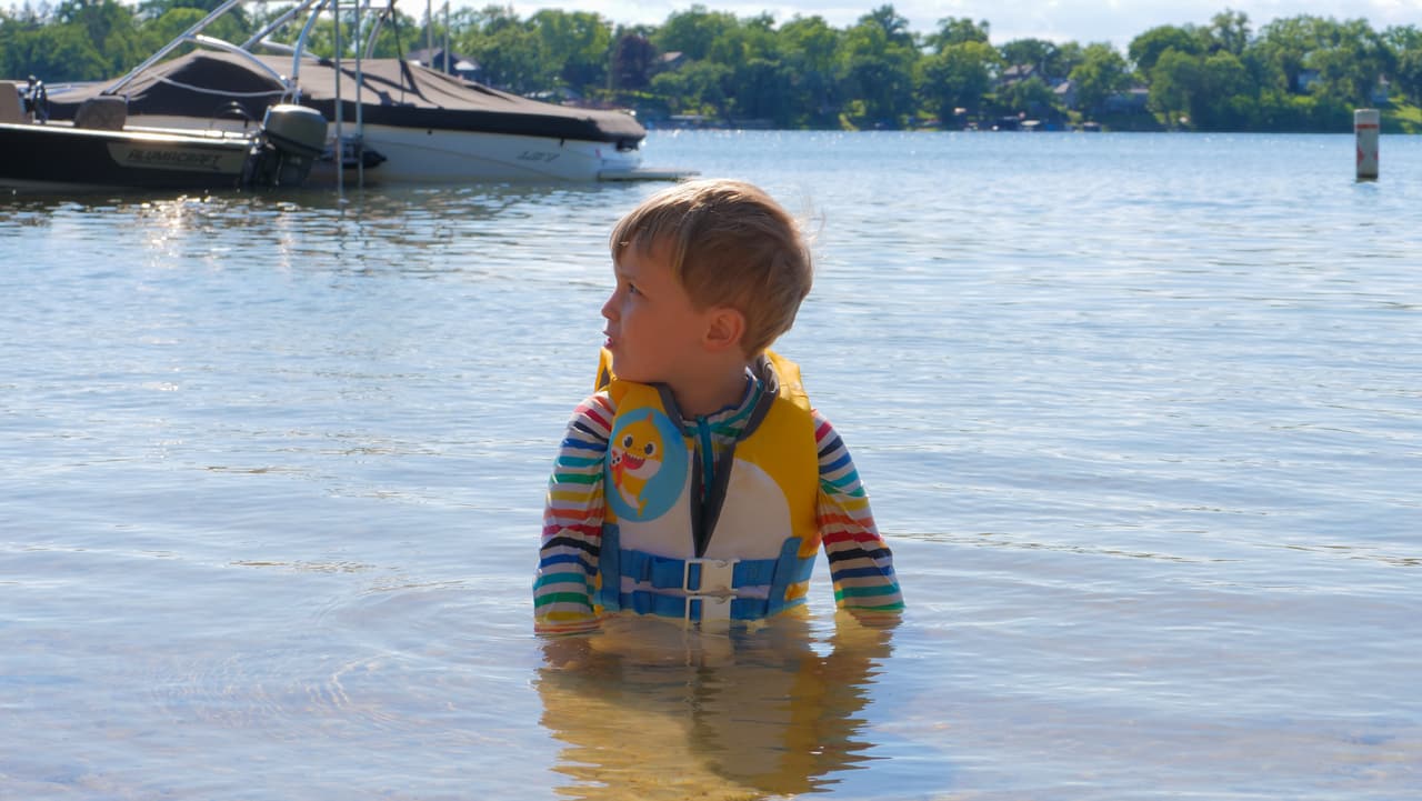 Child in a life jacket wading in the clear, shallow water