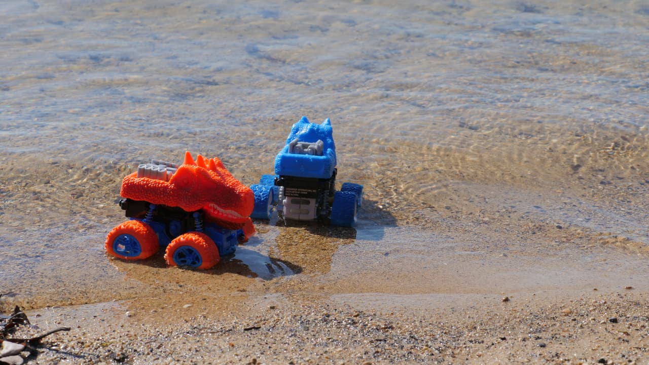 Toy trucks in clear shallow water over sand, showing how clean the lake is