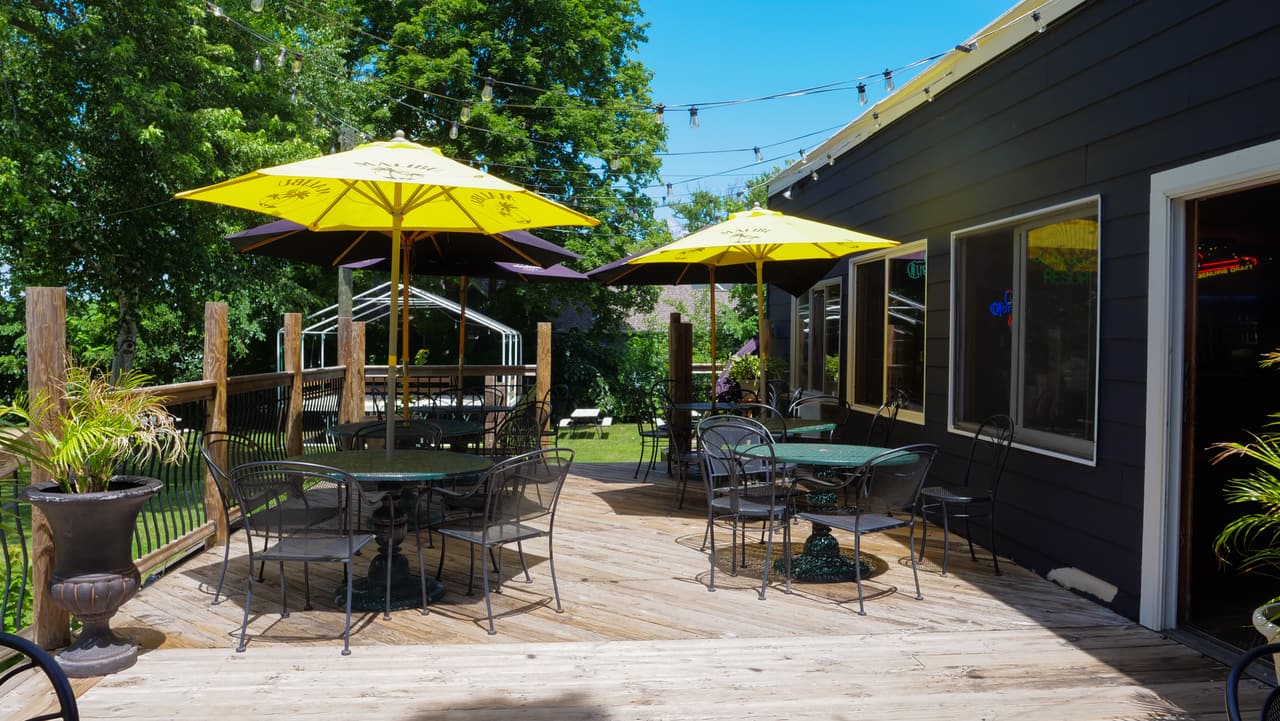 Patio tables under yellow umbrellas outside the bar